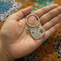 Hand holding a silver keychain with paw prints and an engraved message on a patterned fabric background.